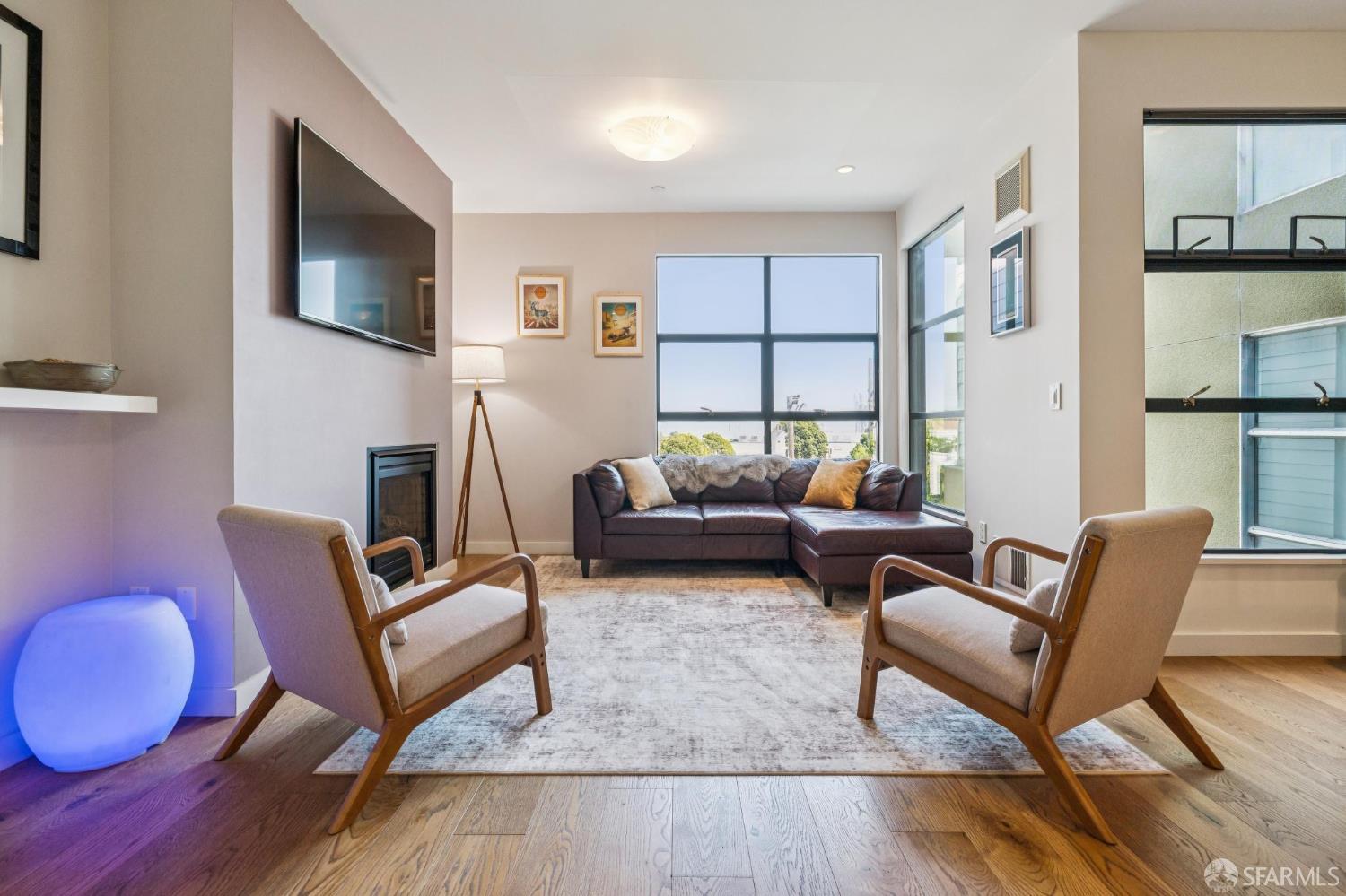 Living room with a leather sectional, two armchairs, fireplace, and large sunny windows.