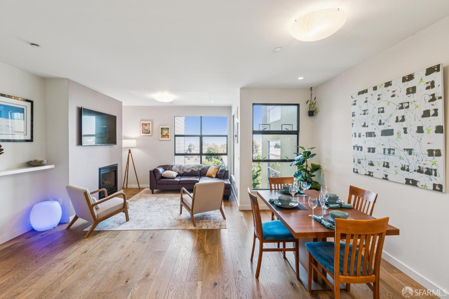 Open-plan living and dining room with wood floors, a fireplace, and large windows.