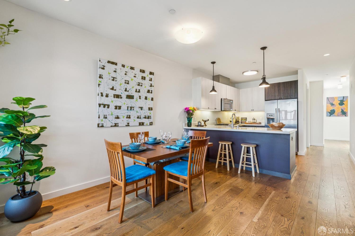 Dining area and modern kitchen with a blue island, pendant lights, and hardwood floors.
