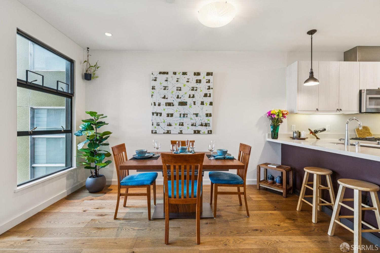 Dining area with a wooden table, blue-cushioned chairs, hardwood floors, and an open kitchen.
