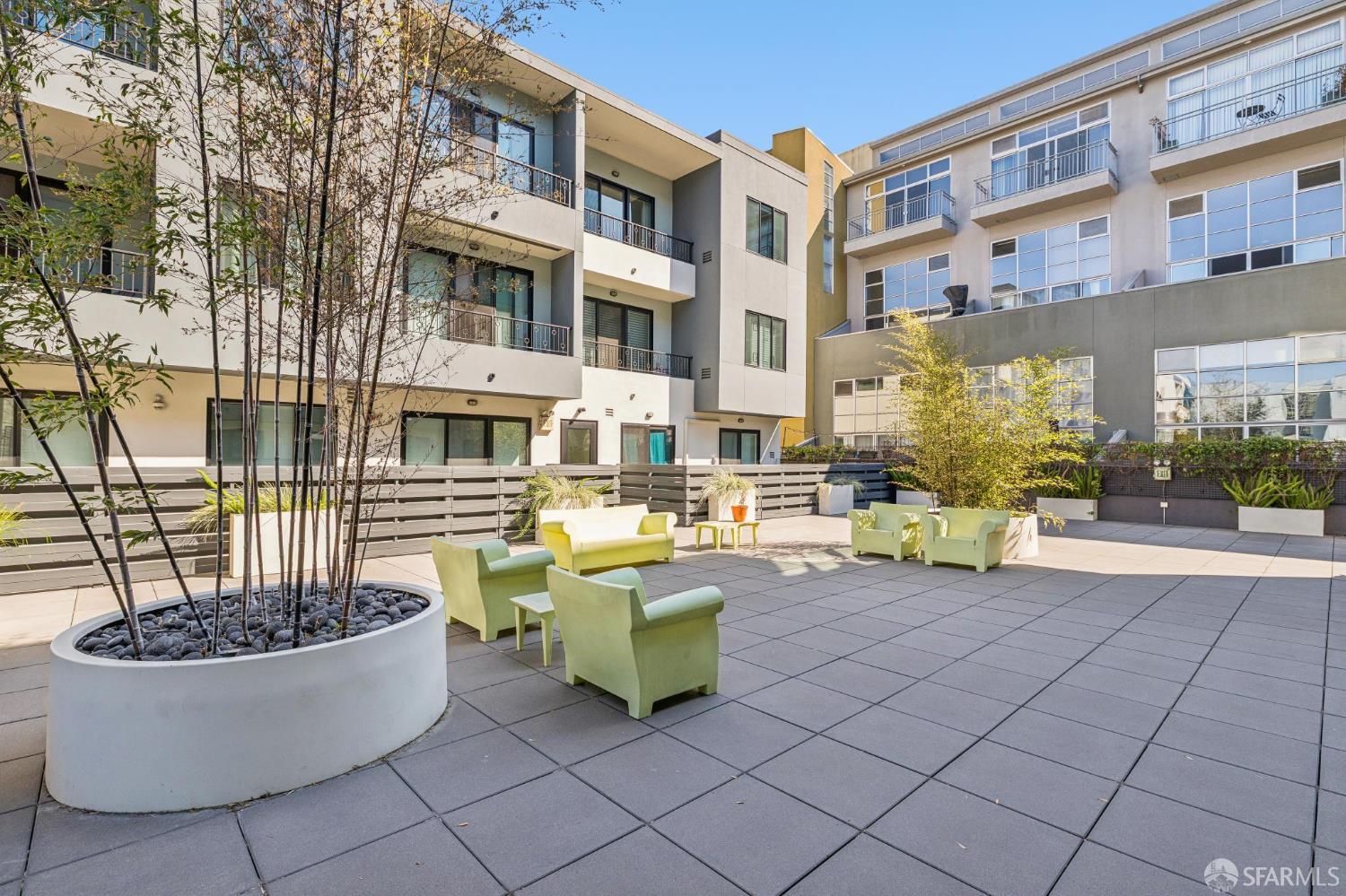 Shared courtyard patio with green lounge seating, raised planters, and modern apartment buildings.