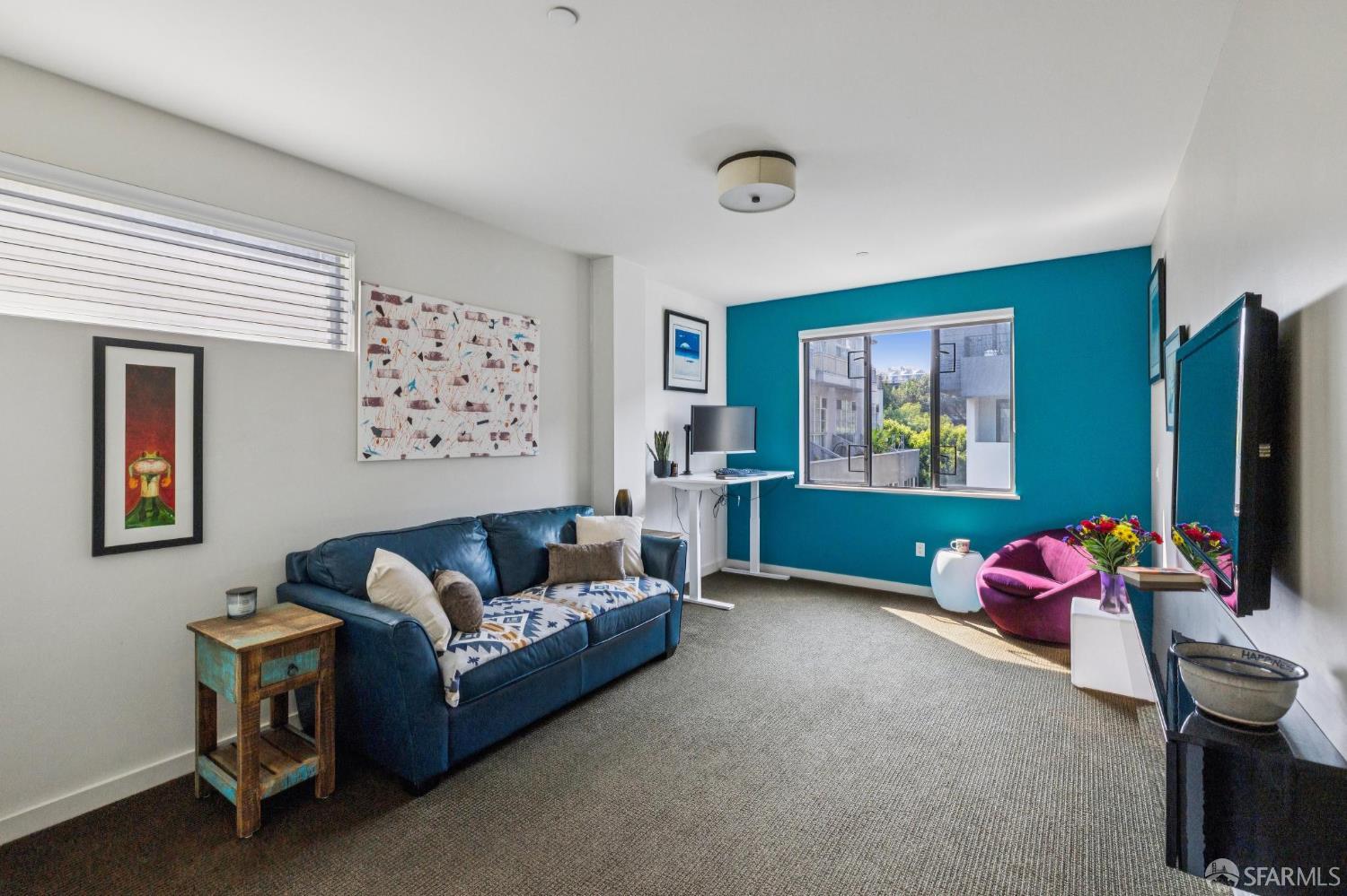Living room with a blue sofa, turquoise accent wall, and window overlooking nearby buildings and greenery.