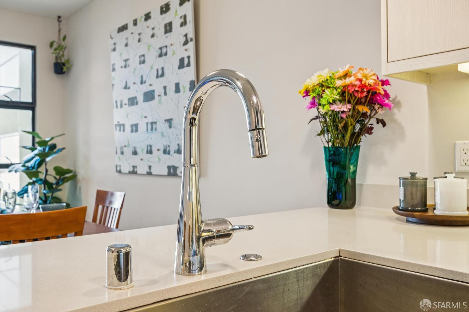 Kitchen island with a chrome gooseneck faucet, colorful flowers, and a dining area beyond.
