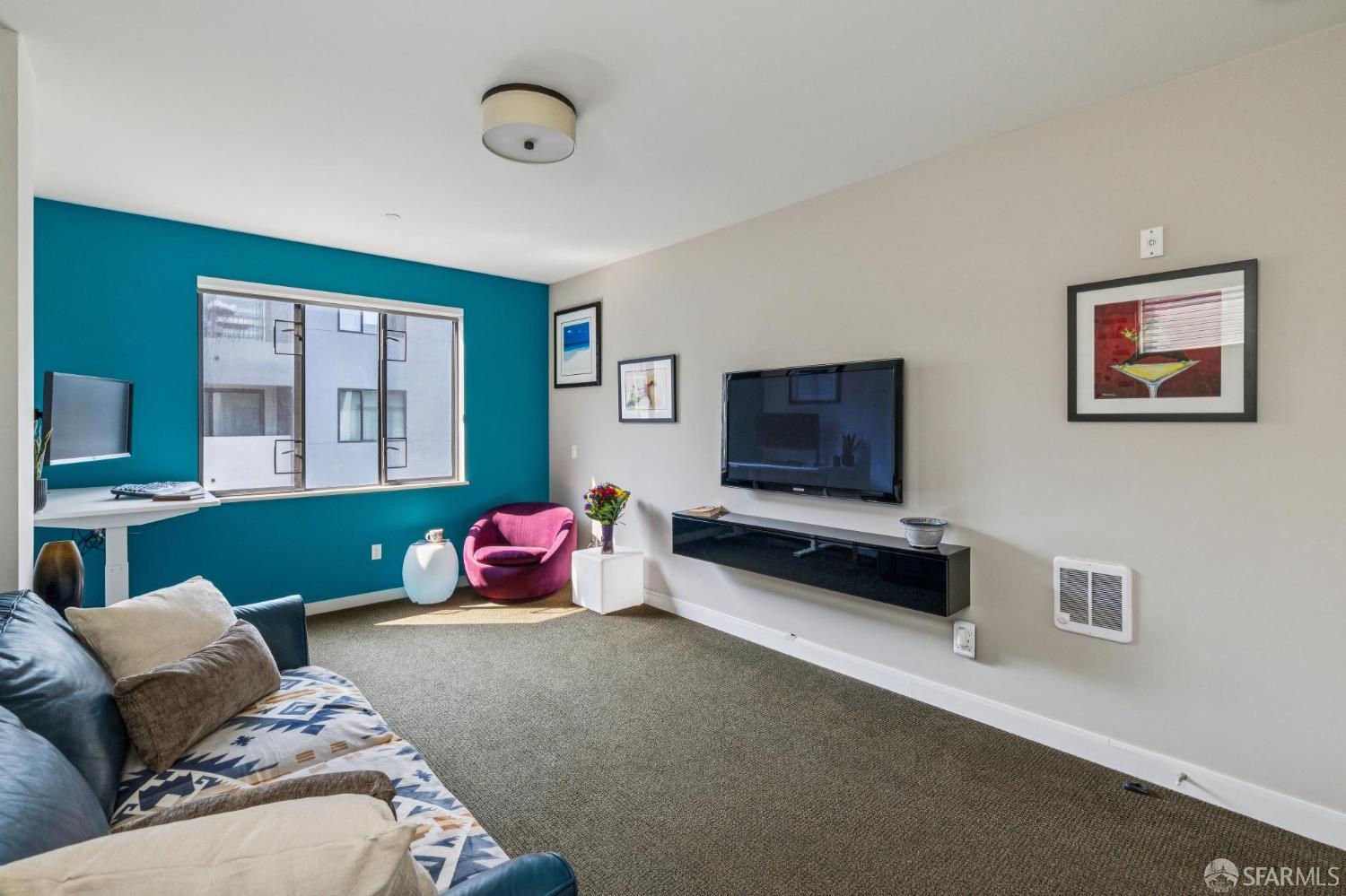 Living room with a teal accent wall, large window, pink armchair, and wall-mounted television.