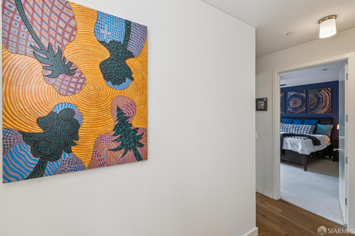 Hallway with colorful abstract wall art looking into a bedroom with a dark blue accent wall.