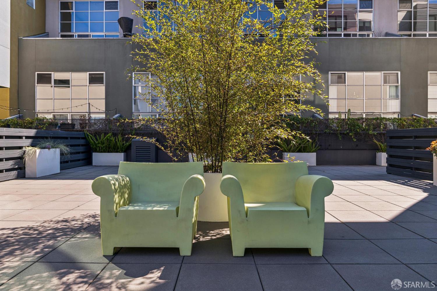 Outdoor terrace with two pale green lounge chairs, planters, and a leafy tree.