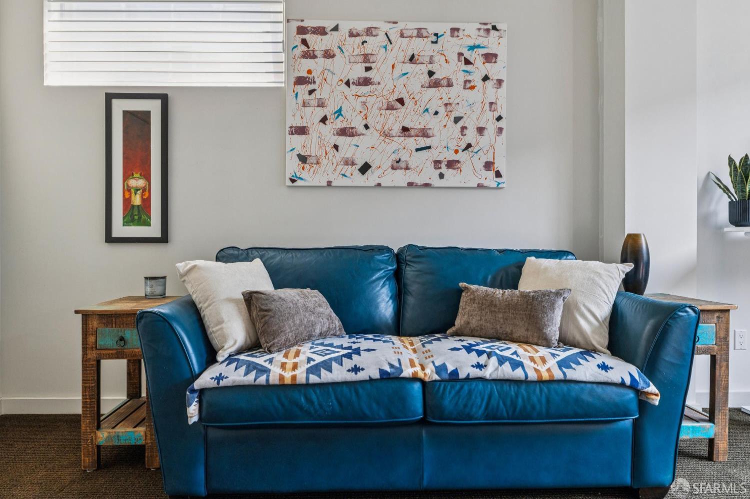 Living room with a blue leather sofa, patterned throw, wooden side tables, and abstract wall art.