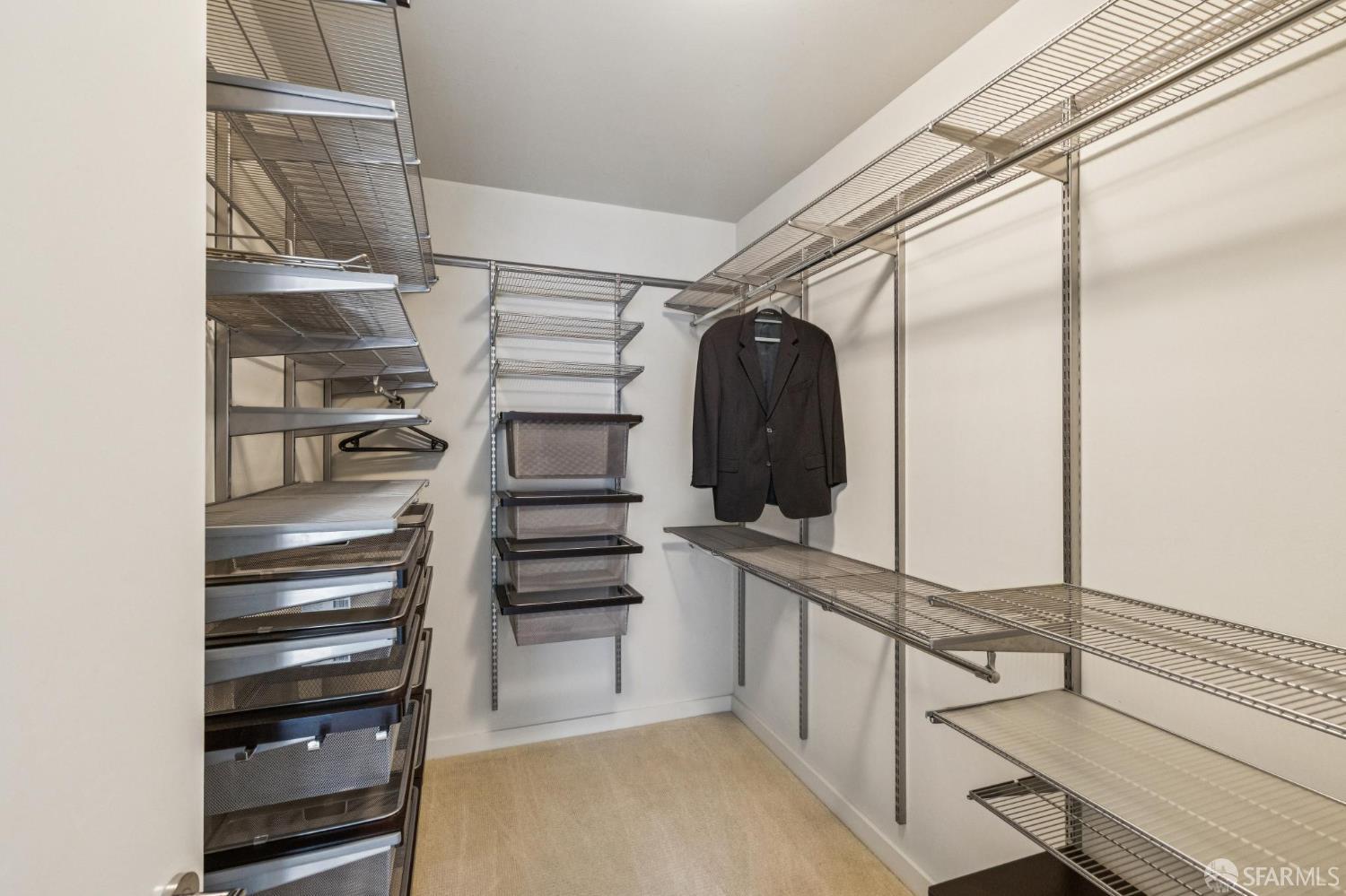 Walk-in closet with extensive wire shelving and a dark jacket hanging on the back wall.
