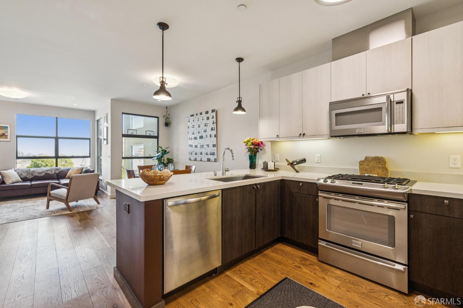Open-plan kitchen with a large island, stainless steel appliances, and a living area beside tall windows.