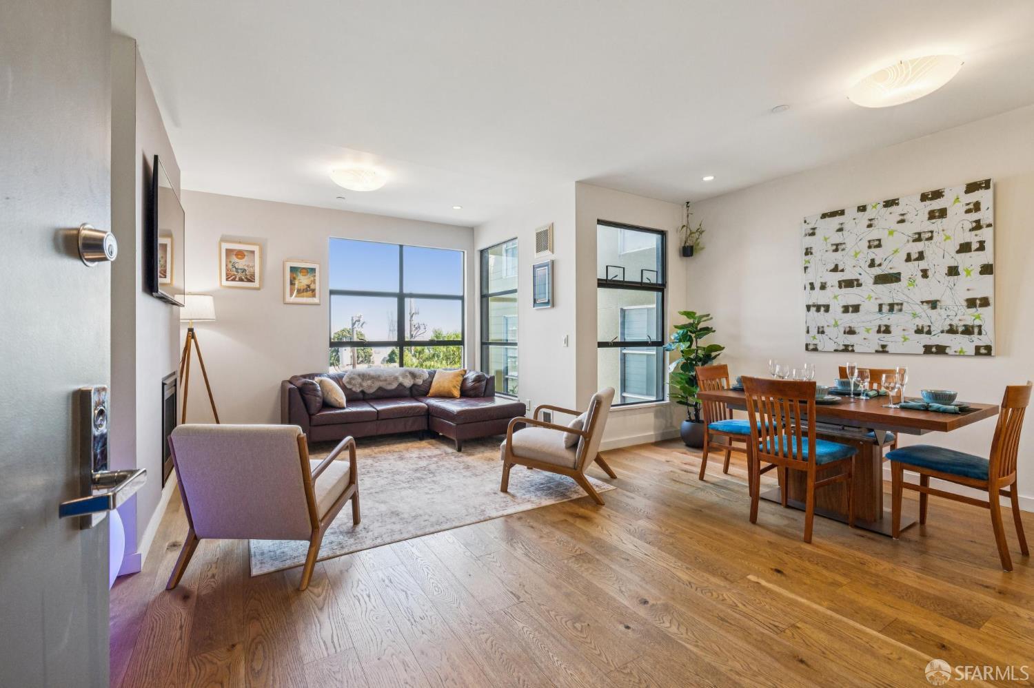 Staged living and dining area with hardwood floors, large windows, and a brown sectional sofa.