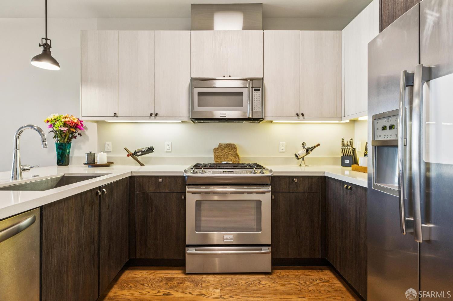 Kitchen with dark lower cabinets, stainless steel appliances, and warm hardwood flooring.