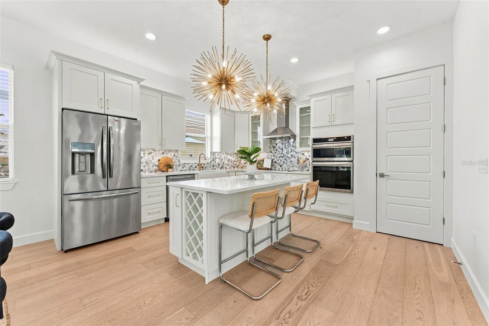 Bright kitchen with white cabinetry, stainless appliances, and a large island beneath gold starburst lights.
