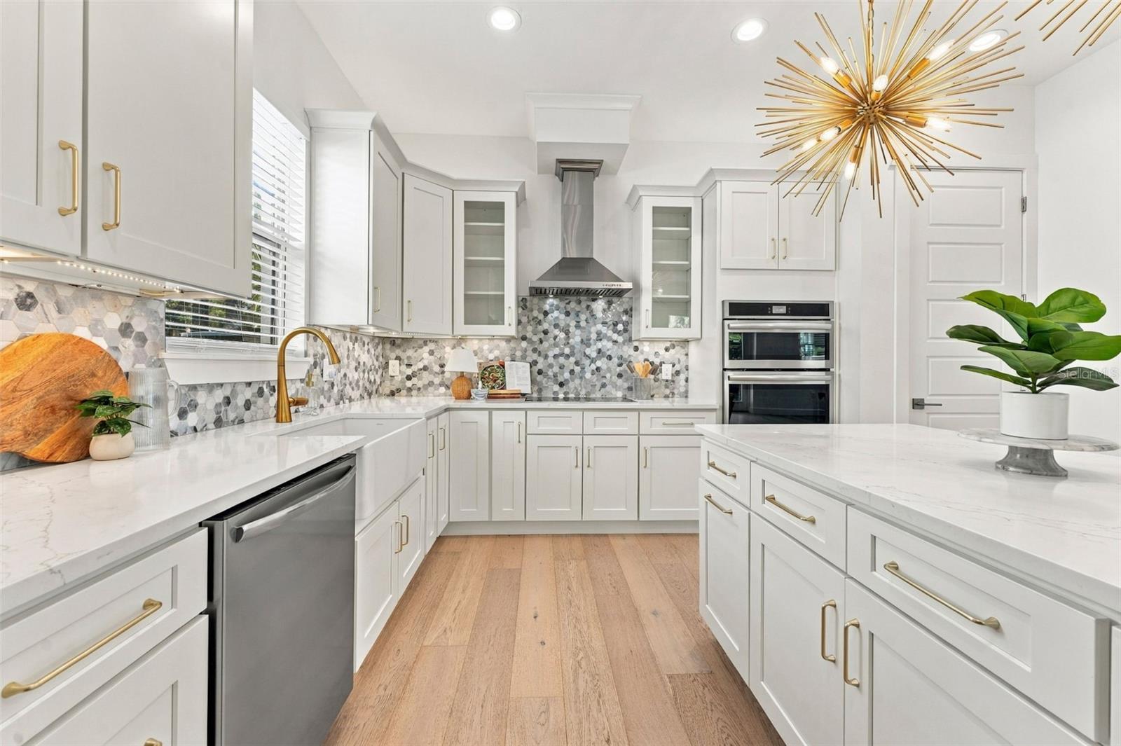 Renovated white kitchen with a gray hexagon backsplash, brass fixtures, stainless appliances, and a gold starburst chandelier.