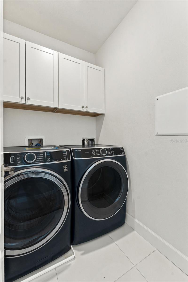 Laundry room with dark front-loading washer and dryer beneath white cabinets.