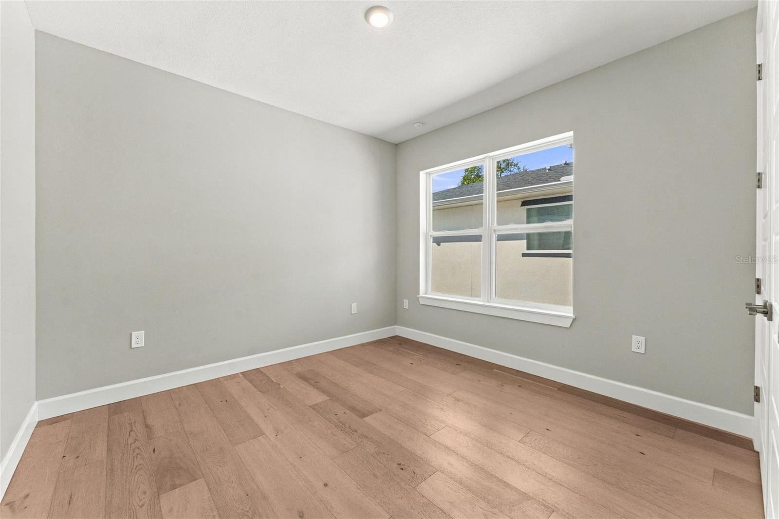 Empty room with light gray walls, a large window, and warm-toned plank flooring.