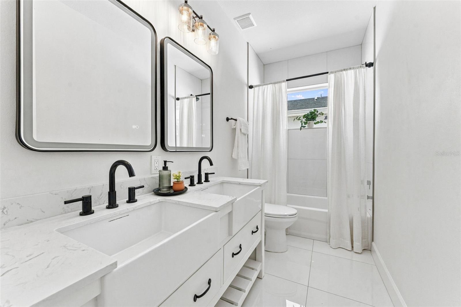 Bright white bathroom with a double vanity, black faucets, and a curtained tub-shower.