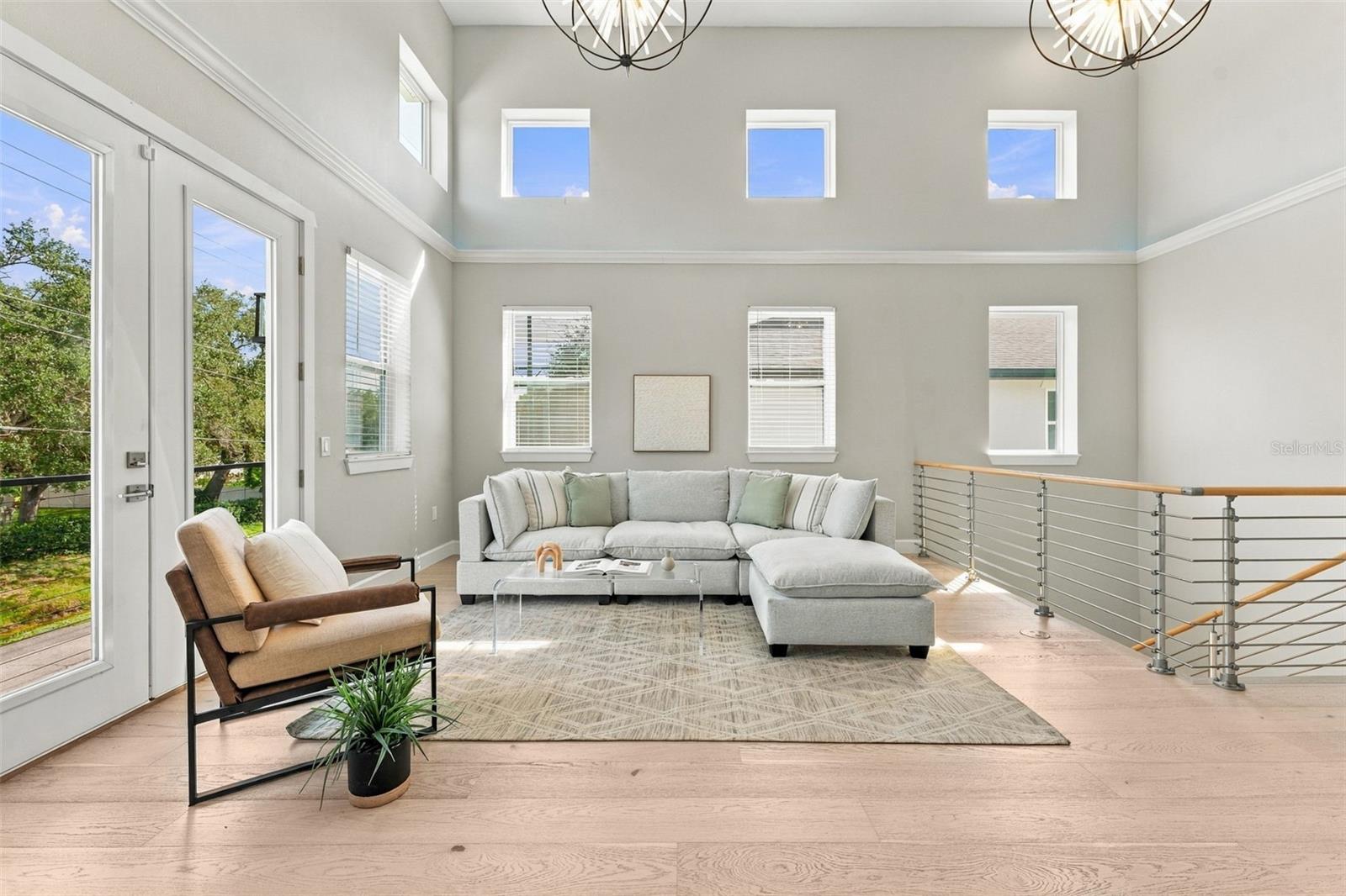 Vaulted living room with a light sectional, clerestory windows, pale wood floors, and a stair railing.