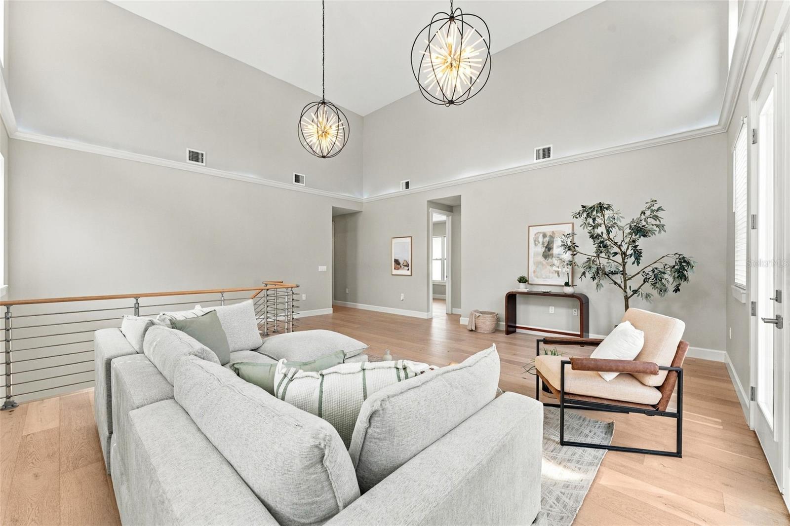 Vaulted living room with a large sectional, globe pendant lights, and light wood floors.