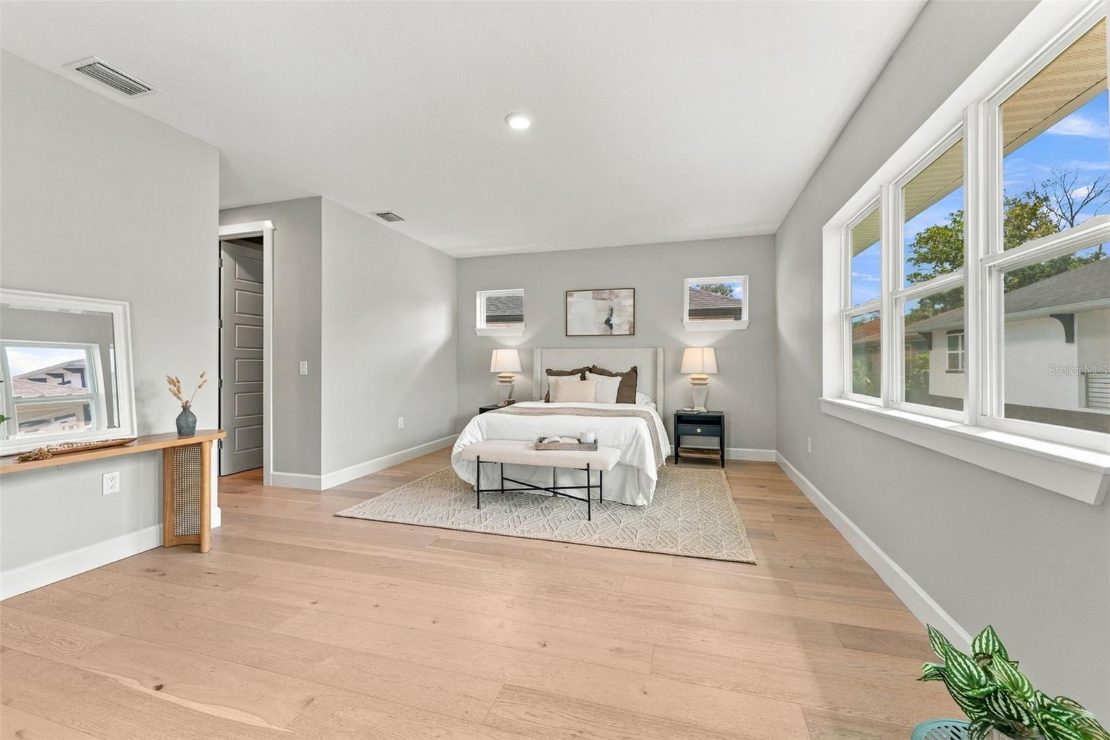 Staged bedroom with a king-size bed, large windows, and light wood flooring.