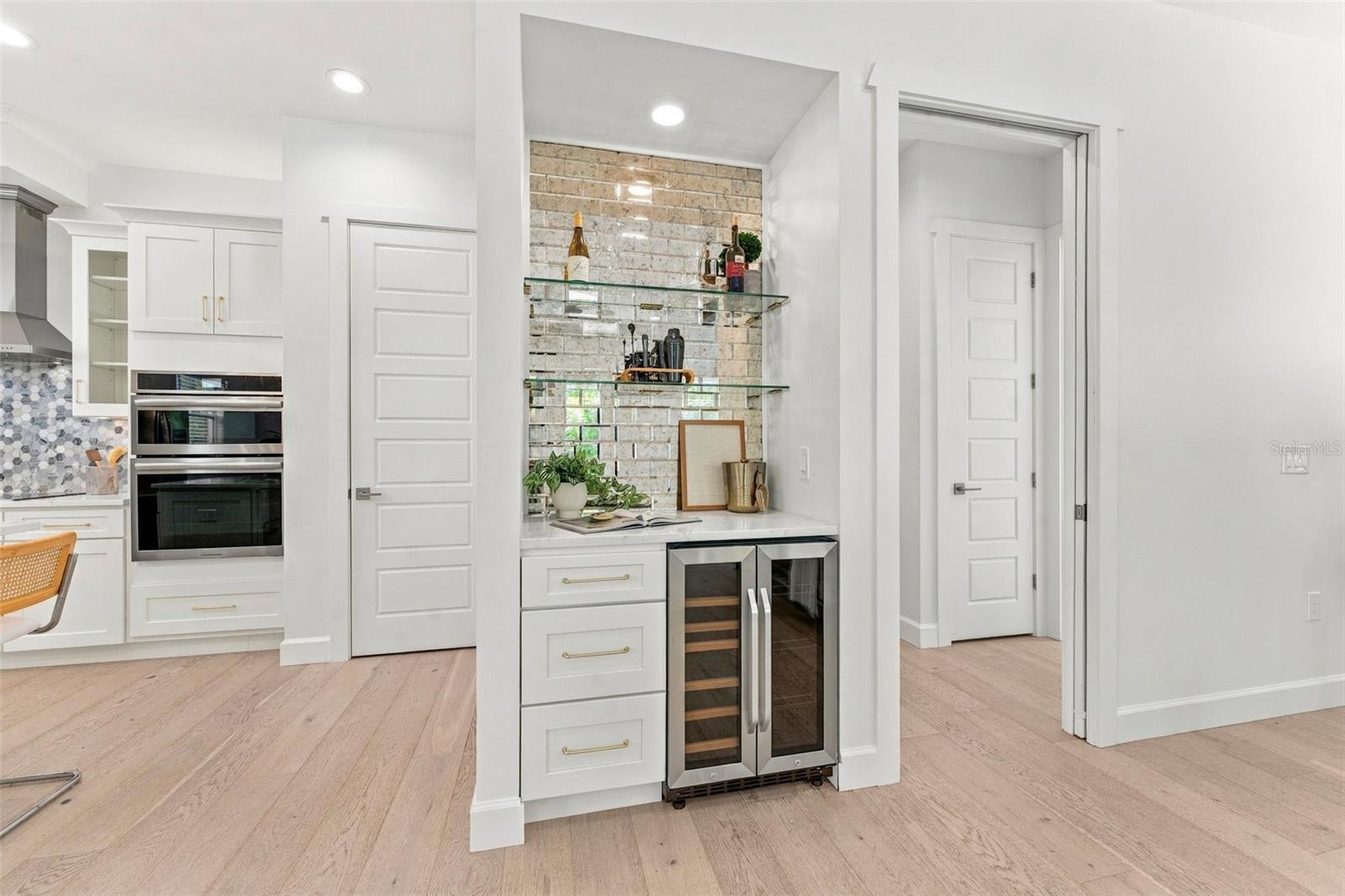 Bright white kitchen with built-in ovens and a brick-backed beverage nook with wine refrigerator.