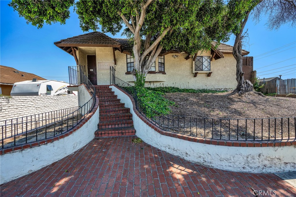 Stucco home with brick entry stairs, curved walls, mature trees, and a raised front yard.