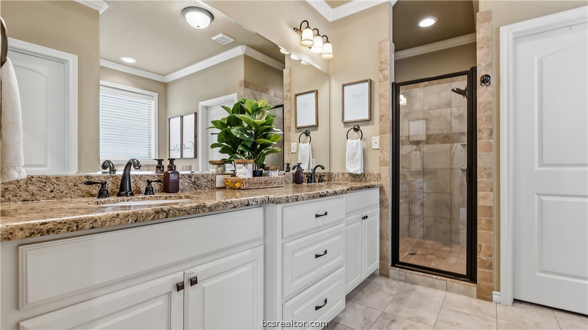 Bathroom with a long double vanity, granite countertop, and glass-enclosed tiled shower.