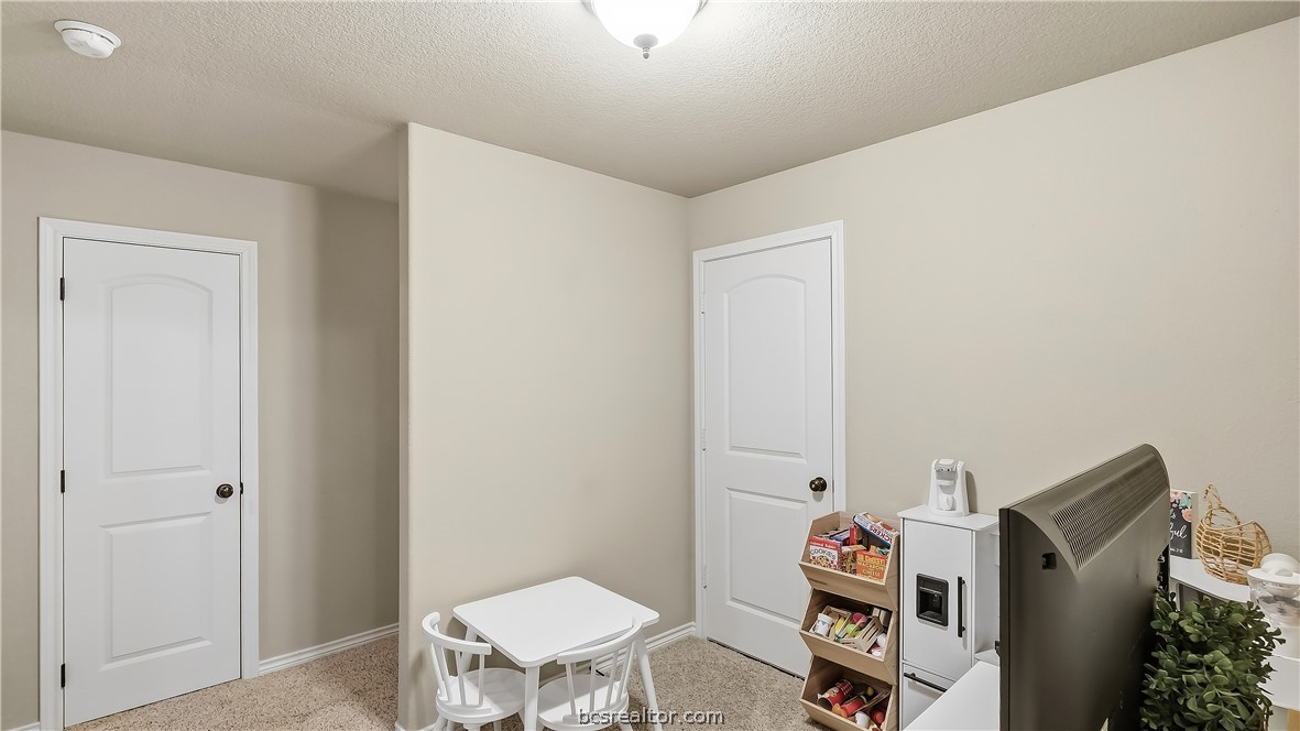 Small playroom with a child-sized table, toy kitchen, and two white doors.