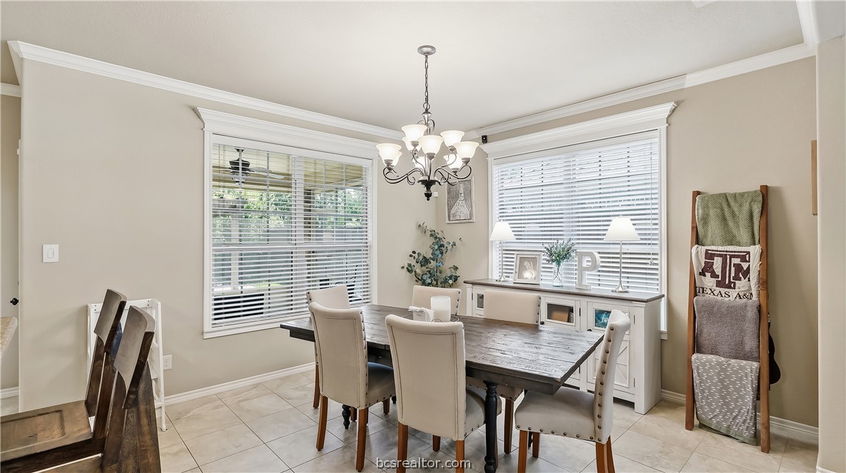 Dining room with a dark wood table, upholstered chairs, chandelier, and large windows with blinds.