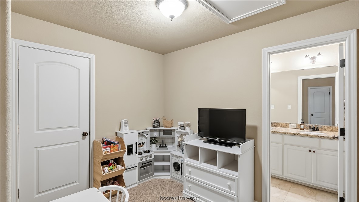 Furnished playroom with a toy kitchen, small table, and television beside an open bathroom doorway.
