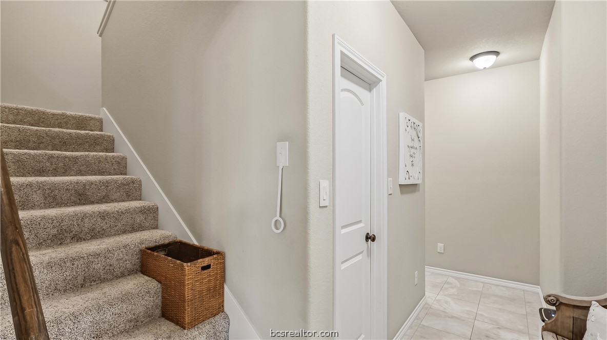Carpeted staircase beside a white door and tiled hallway.