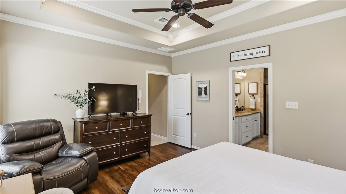 Bedroom with a tray ceiling, dark wood dresser, leather recliner, and doorway to an ensuite bathroom.