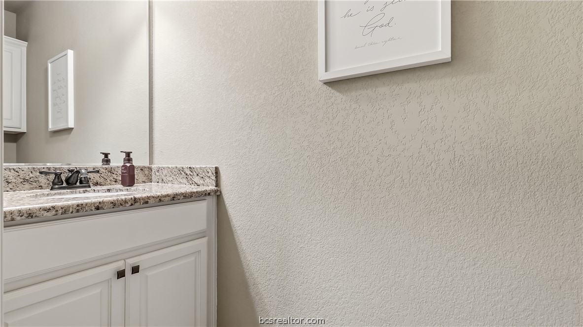 Bathroom vanity with a granite countertop, white cabinetry, and framed wall art.