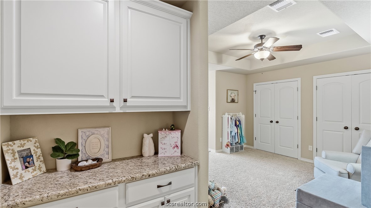 Carpeted bedroom with white built-in cabinets, a granite counter, and double closets.