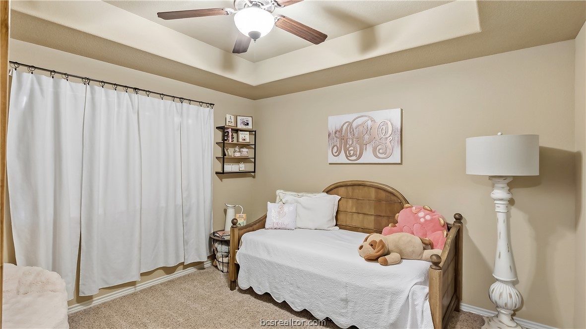 Bedroom with a wooden daybed, plush toys, white curtains, and a tray ceiling.