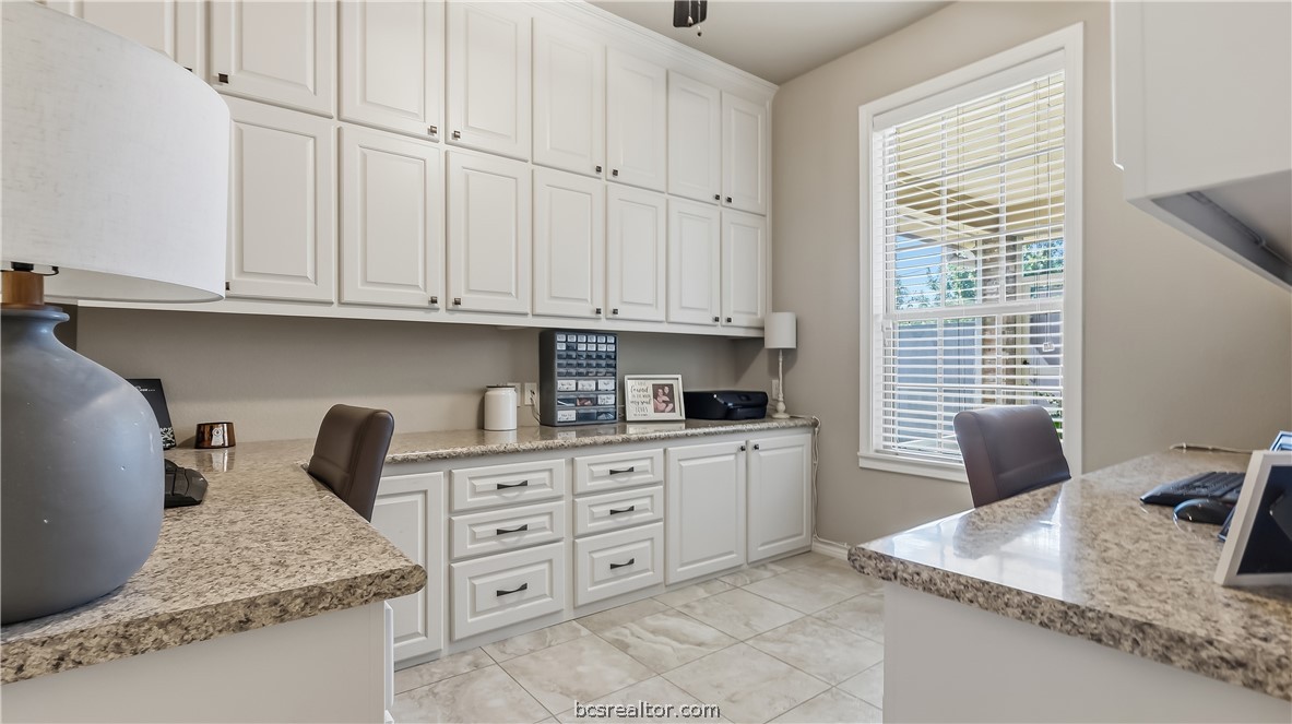 Home office with white built-in cabinets, granite counters, and a large window.