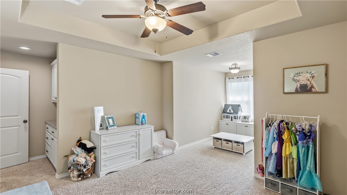 Children’s playroom with carpet, toy storage, dress-up costumes, and a ceiling fan.
