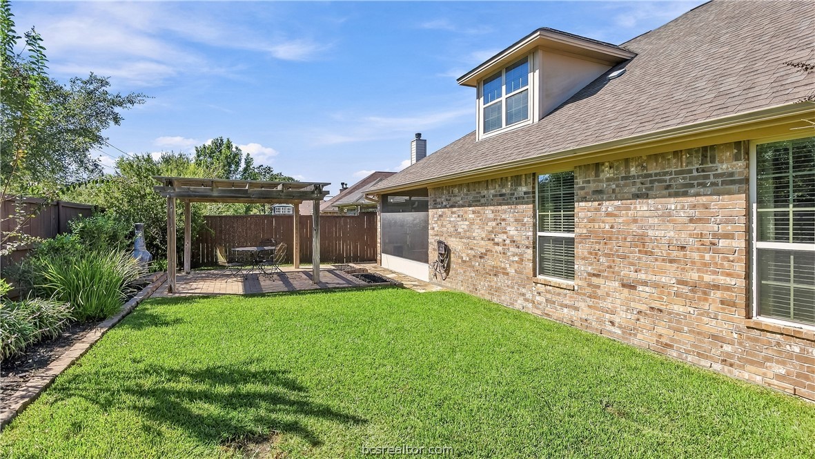 Brick home backyard with a broad green lawn, fenced patio, and wooden pergola.