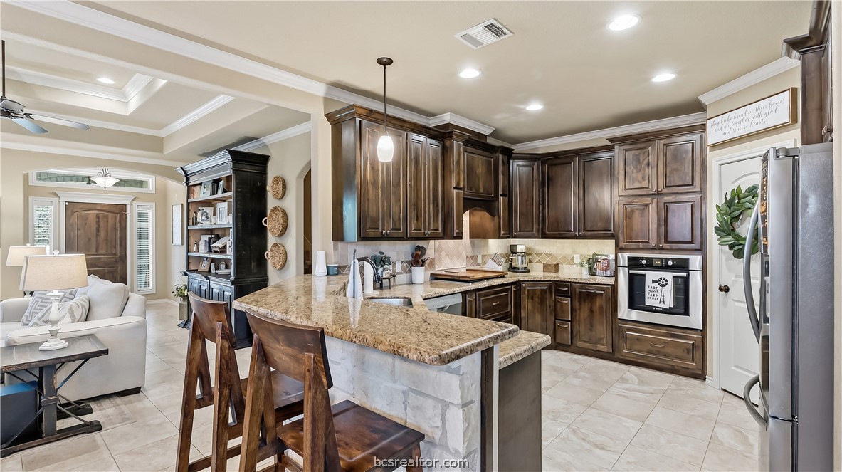 Kitchen with dark wood cabinets, granite island, and seating opening to a living area.