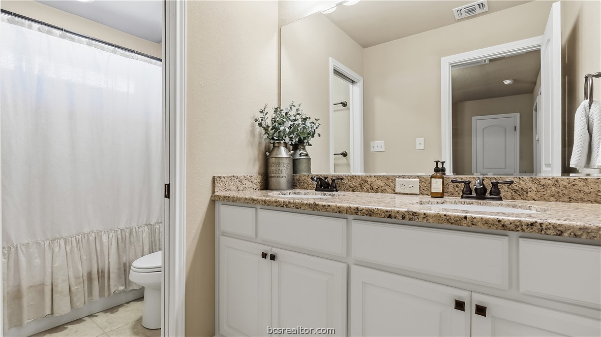 Bathroom with a double-sink vanity, granite countertop, and adjacent tub-shower behind a curtain.