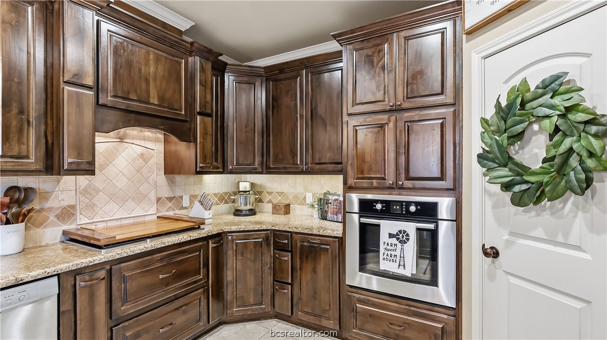 Kitchen with dark wood cabinets, granite counters, tile backsplash, and stainless steel appliances.