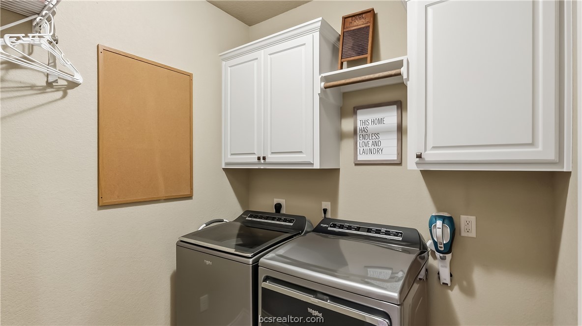 Laundry room with gray washer and dryer, white cabinets, and a framed laundry sign.