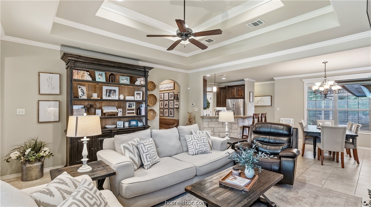Living room with a tray ceiling, dark built-in shelving, and an open view into the kitchen and dining area.