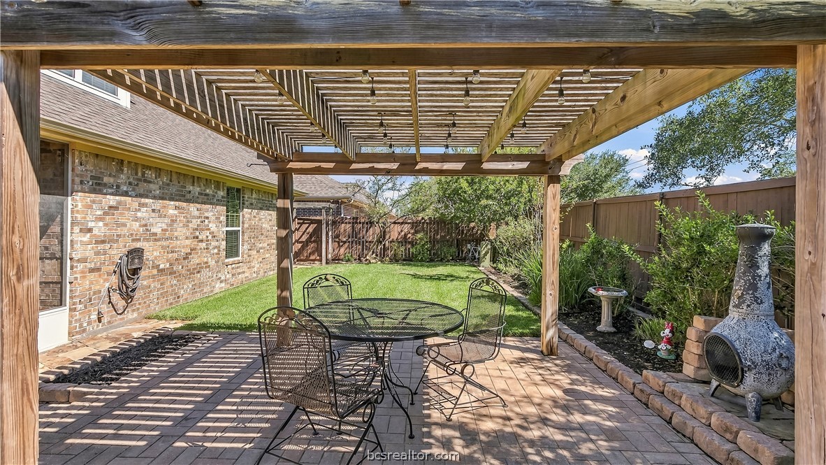 Backyard patio with a wooden pergola, metal dining set, and outdoor fireplace.