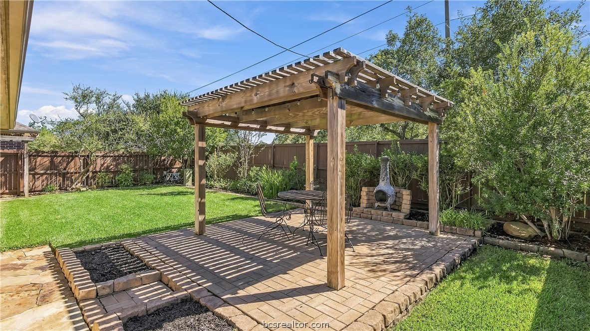 Backyard patio with a timber pergola, outdoor fireplace, and metal dining set.