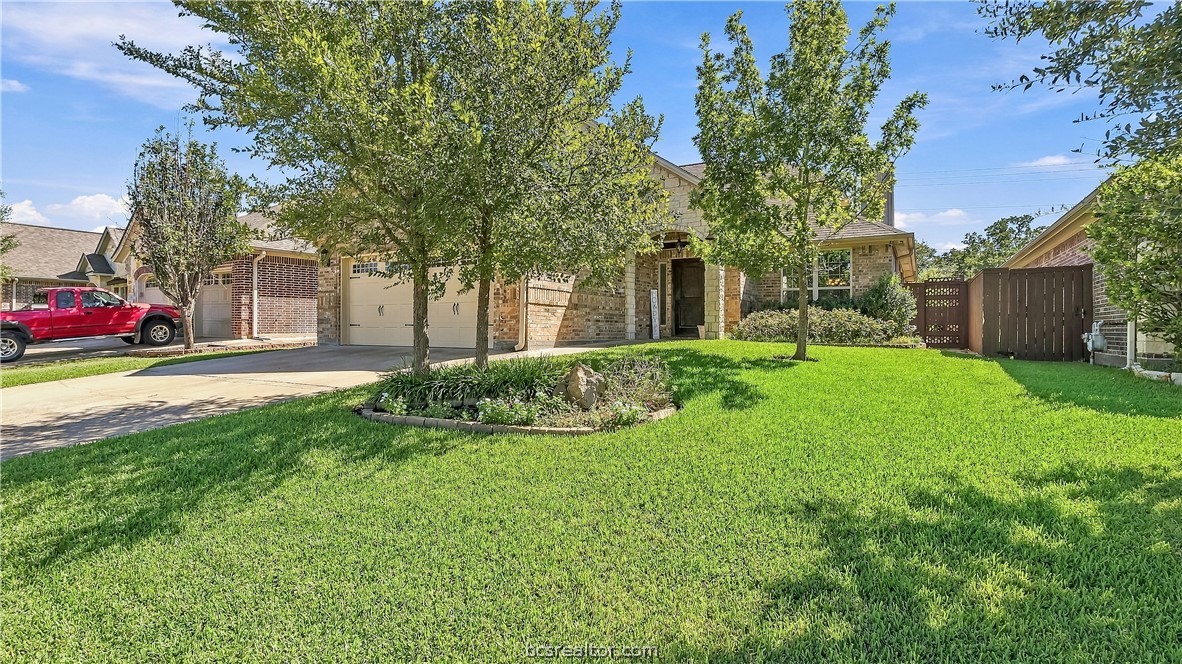 Brick home with a two-car garage, landscaped lawn, and mature trees in front.
