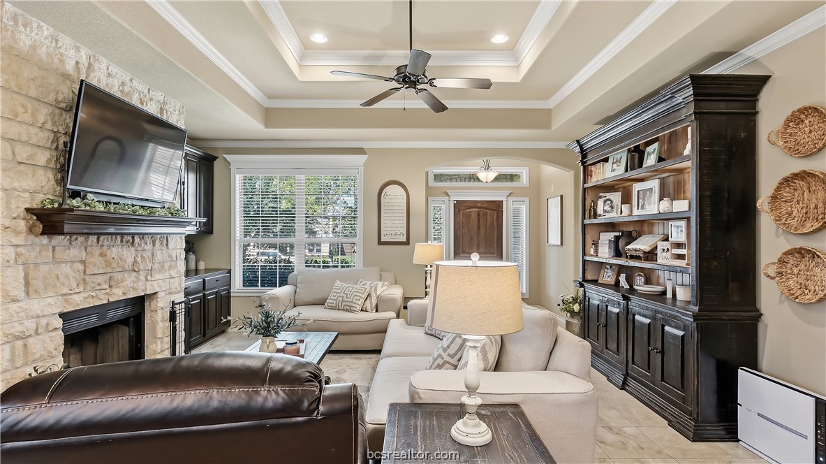 Living room with a stone fireplace, built-in dark wood shelving, and a tray ceiling.