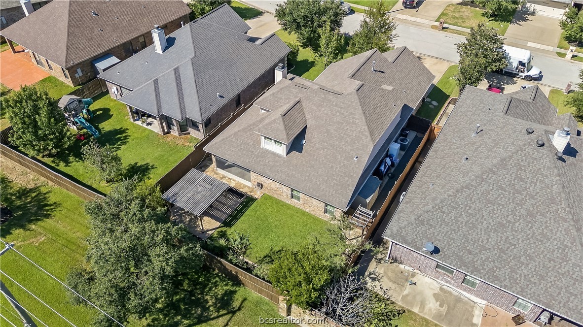 Aerial view of a brick home with a fenced backyard, lawn, and pergola.