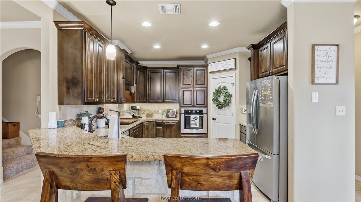 Kitchen with dark wood cabinets, granite island, stainless steel appliances, and two wooden barstools.