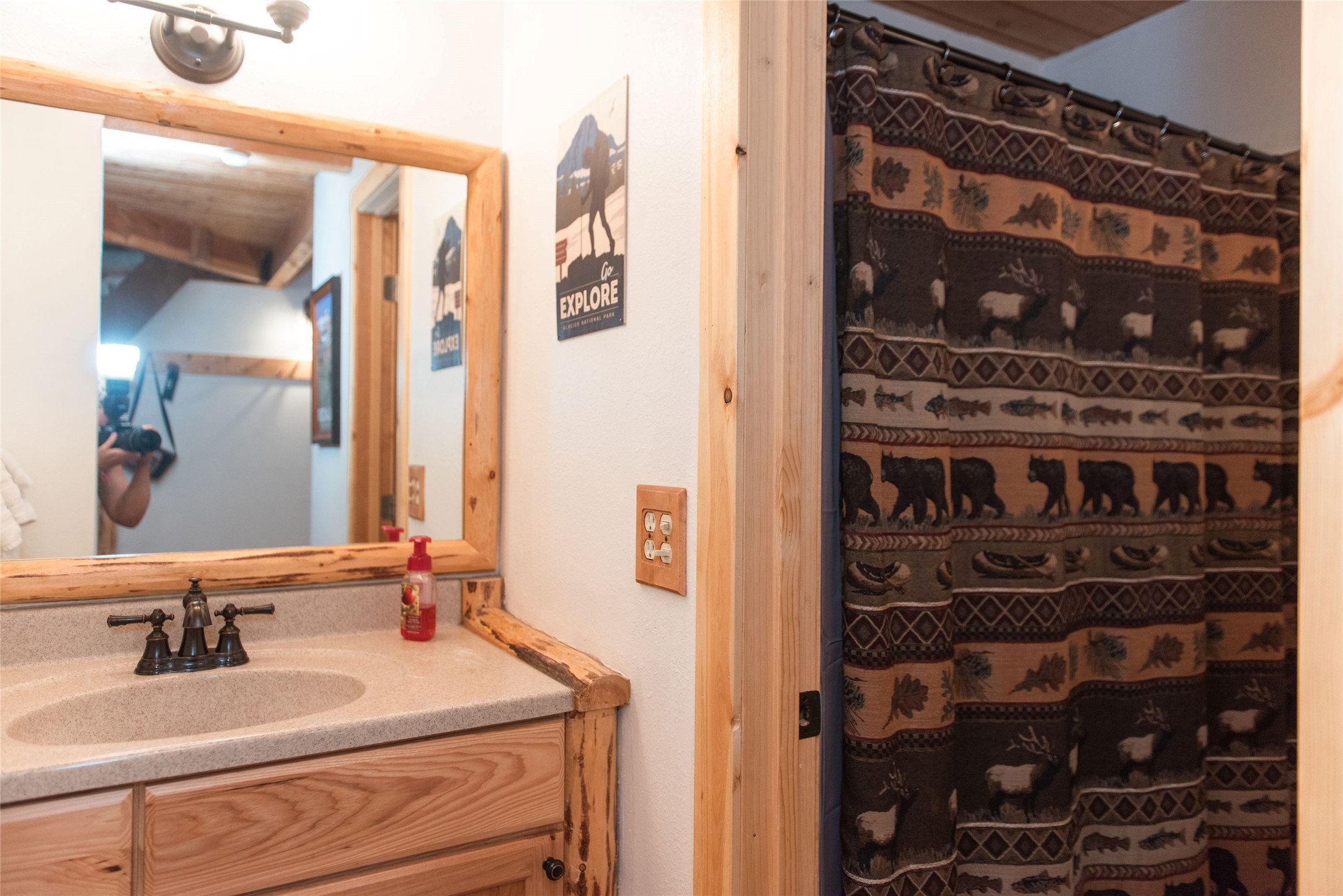 Bathroom vanity with rustic wood trim, large mirror, and wildlife-patterned shower curtain
