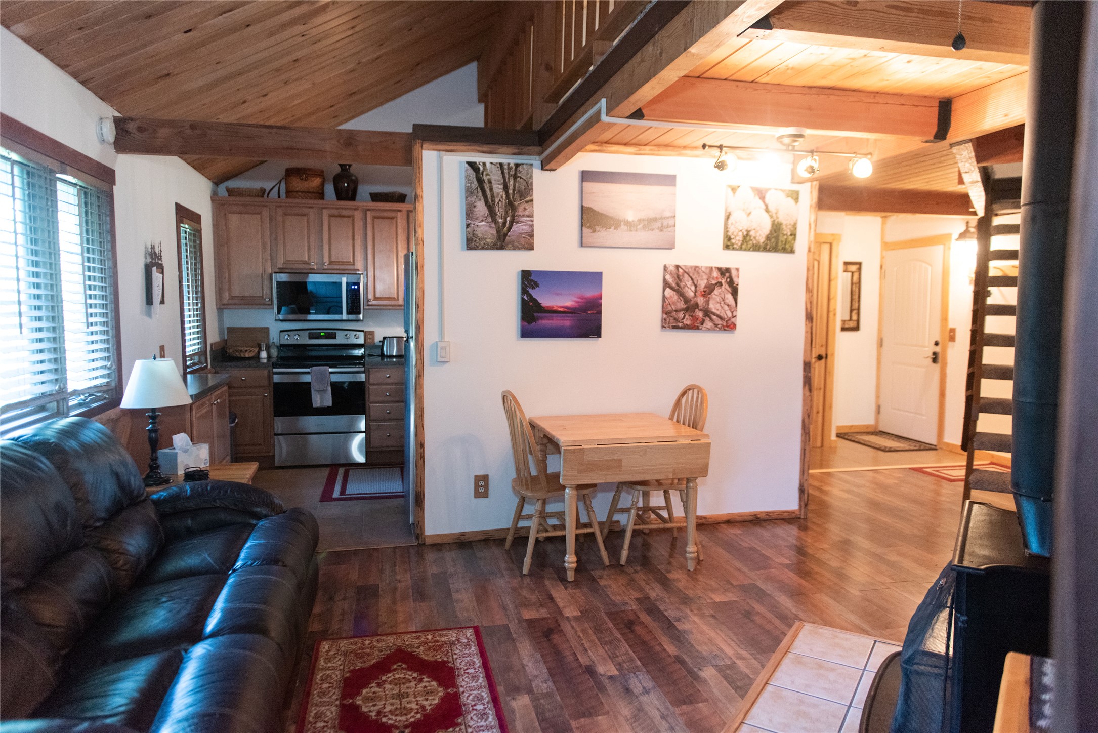 Open-plan condo living and dining area with a vaulted wood ceiling, leather sofa, and compact kitchen.
